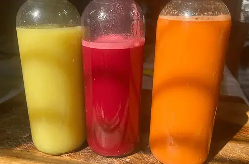Three colorful juices in bottles on a wooden table.