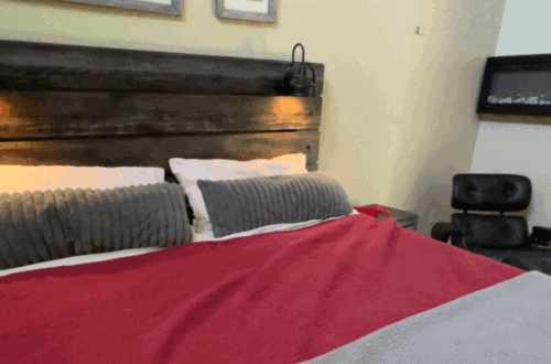 Cozy modern bedroom with a wooden headboard, gray pillows, and a red and gray bedspread. Perfect for.