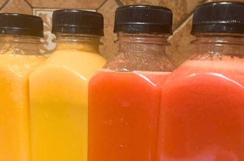 Four bottles of juice or smoothie with black caps in yellow, orange, and pink colors.