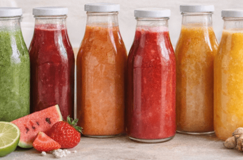 Colorful smoothies in glass bottles with fresh fruit and ginger on a wooden surface.