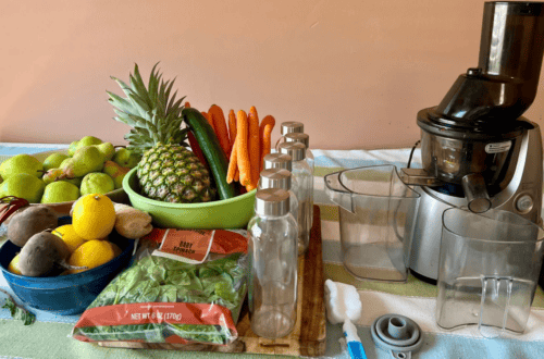 Juicing setup with fresh fruits, vegetables, and a juicer on a kitchen counter.