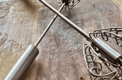 Two push whisks resting on a rustic wooden table.