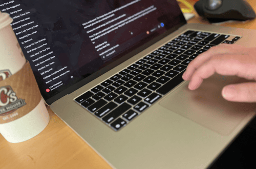 Person typing on a laptop with a coffee cup nearby, focused on digital content creation.