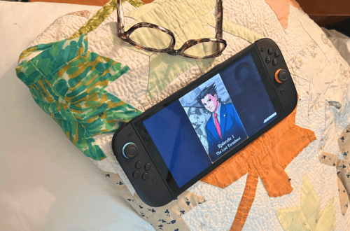 Gaming console displaying anime scene with glasses on quilted bedspread.