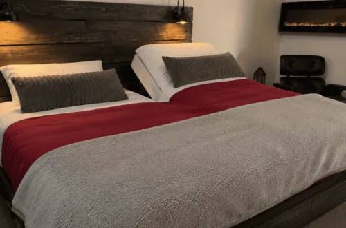 Cozy bedroom with wooden headboard, red and gray bedding, and ambient lighting.