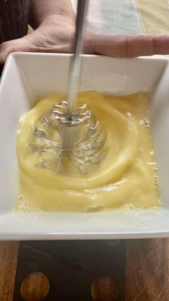 Close-up of a hand-held using the push whisk as a egg beater mixing eggs in a white bowl.
