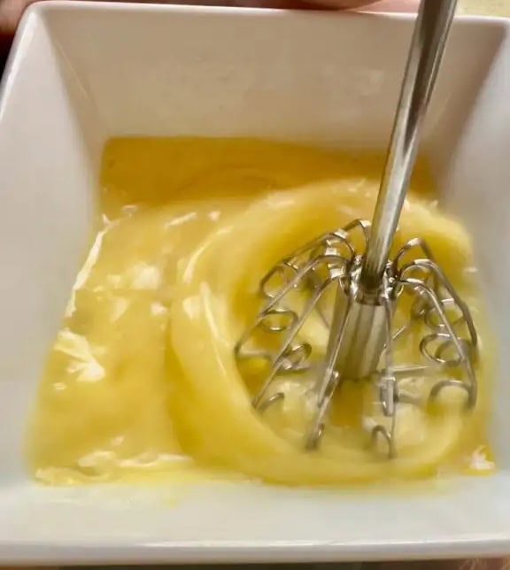 Creamy homemade butter being churned in a white container with a hand mixer.
