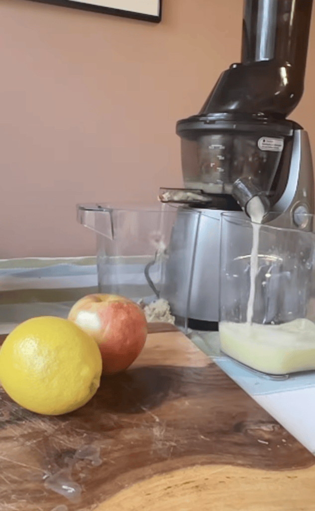 Juice maker on countertop with lemon, apple, and ingredients for fresh juice.