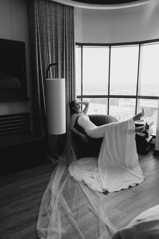 Bride relaxing playfully in a chair by the window at Brookstreet Hotel, in black and white