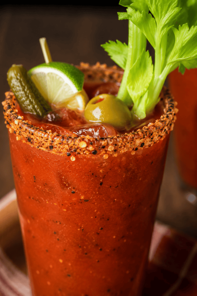 Close-up of a Bloody Mary with celery, lime, and olives in a salted rim glass.