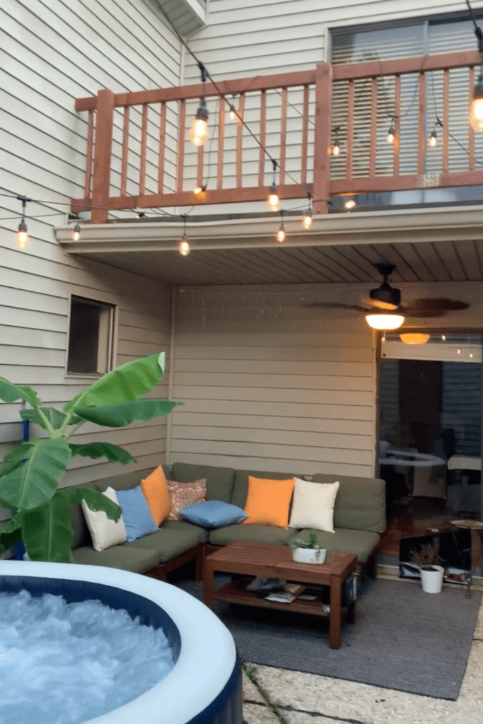 Outdoor patio with string lights, sofa, and hot tub at dusk.