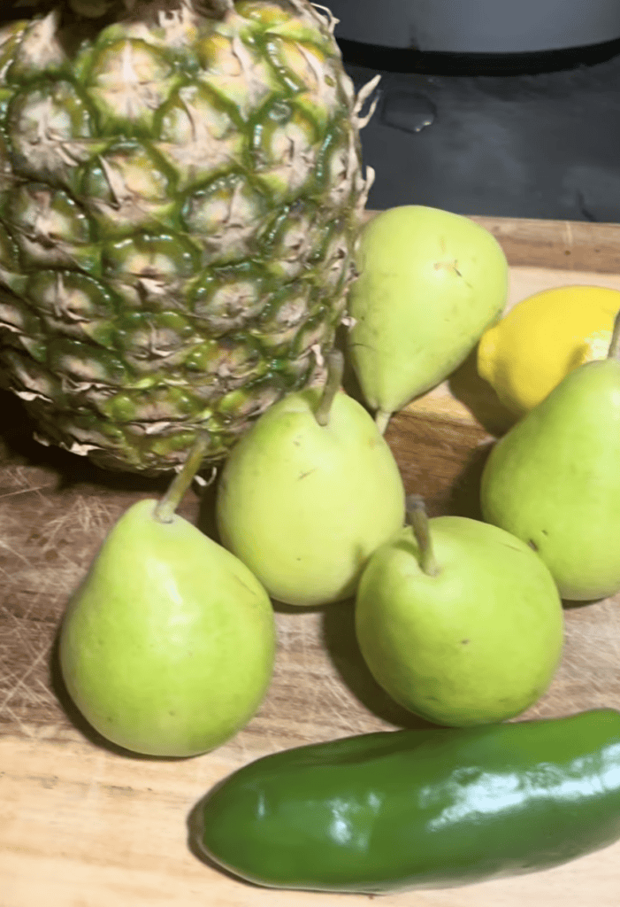 Assorted fresh fruits including pineapple, pears, and cucumber on wooden cutting board.