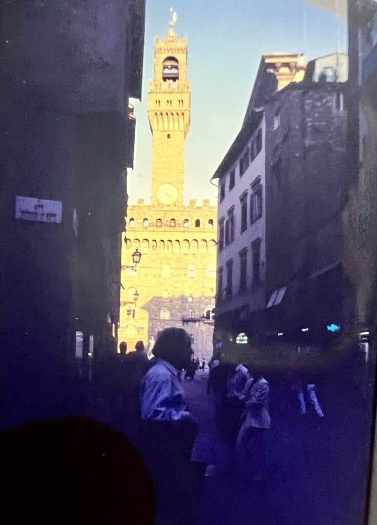 People walking in Florence's historic square with the Palazzo Vecchio tower.