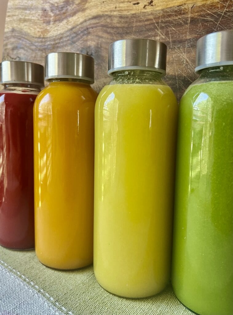 Vibrant bottles of juice in red, yellow, and green on a wooden surface.