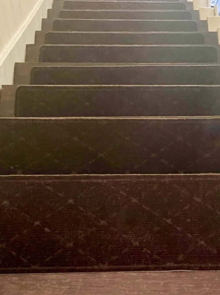 Staircase with black carpet runners and wooden steps, viewed from above.