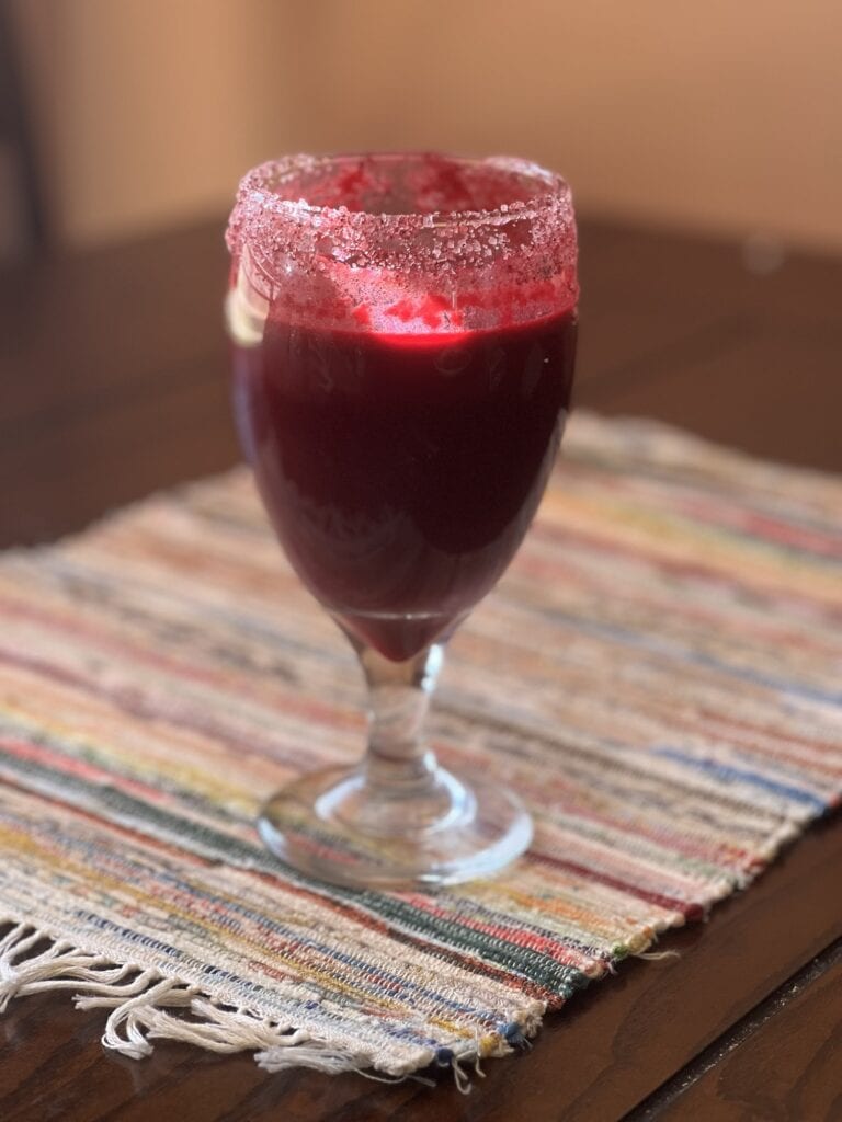 Gourmet berry cocktail with sugared rim in a tall glass, served on a colorful woven placemat.