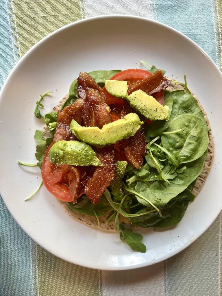 Healthy salad with avocado, tomato, bacon, and greens on a white plate.