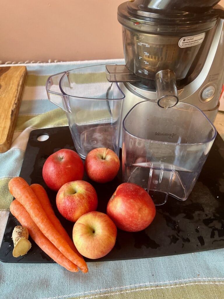 Fresh apples and carrots with a juicer on a kitchen counter.