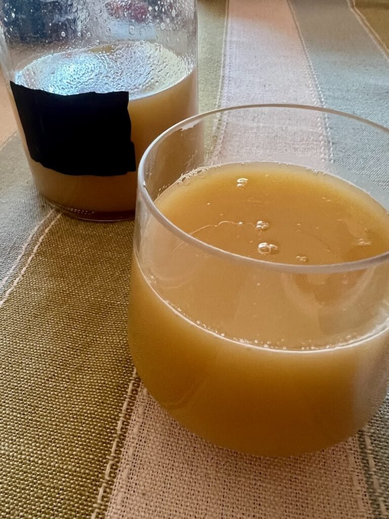 Two glasses of fresh juice on a table, one in a glass cup and the other in a tumbler.