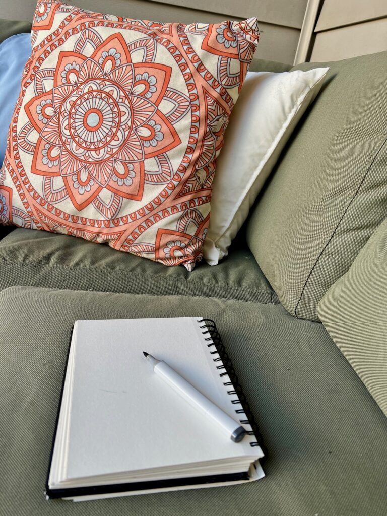 Colorful mandala-patterned pillow on a green couch with a notebook and pen.