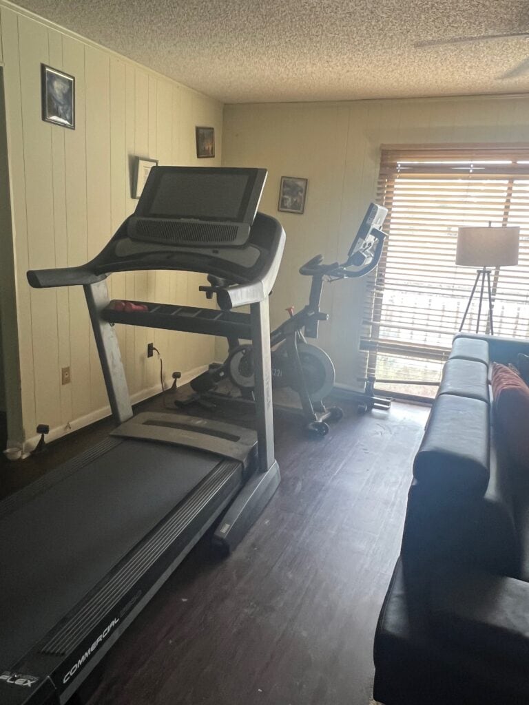 Home gym setup with treadmill and exercise bike near window with blinds.
