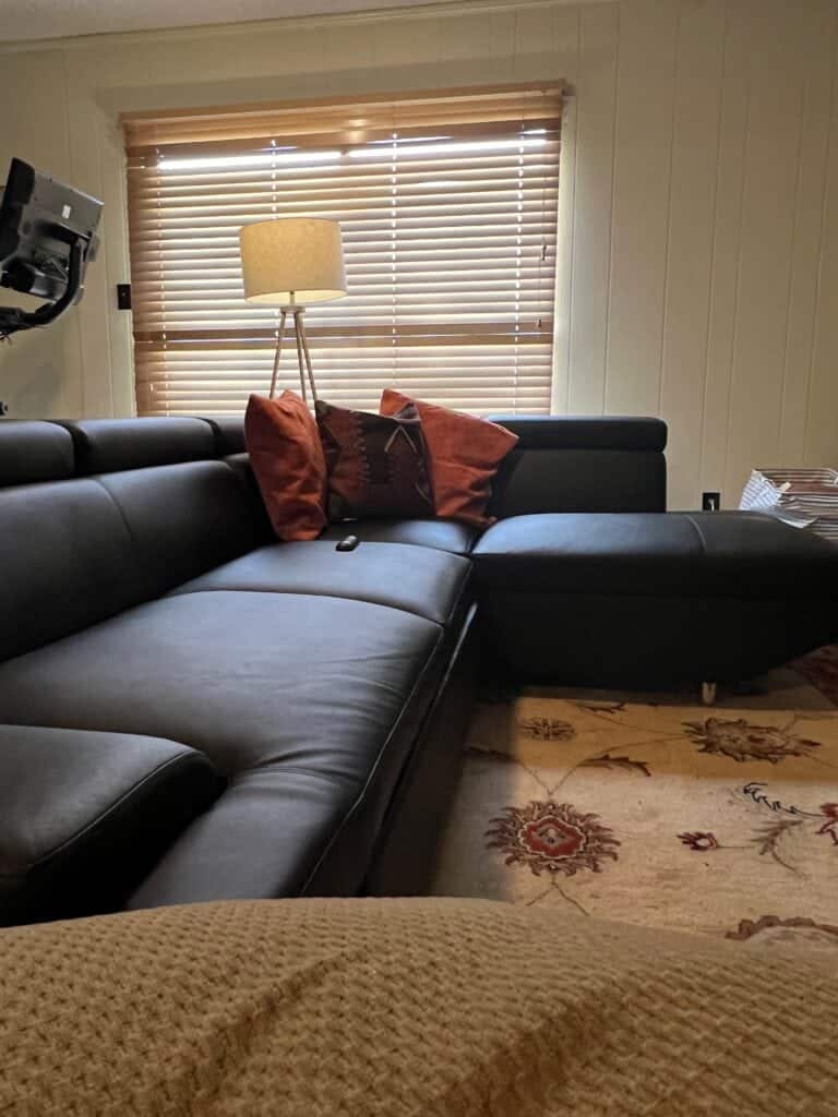 Cozy living room with black leather sectional and wooden blinds.