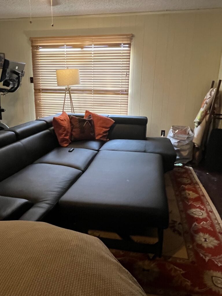 Cozy living room with black sectional sofa, window with blinds, and decorative pillows.