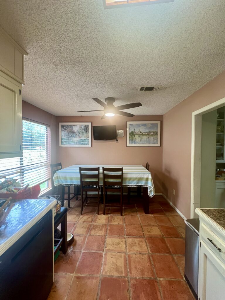 Bright dining room with table, chairs, and wall art, featuring a ceiling fan and large window.