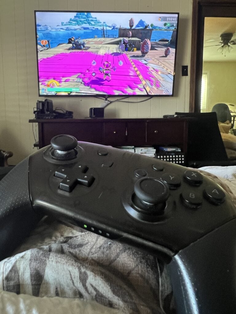 Gaming controller in foreground, TV screen showing a colorful game in background.