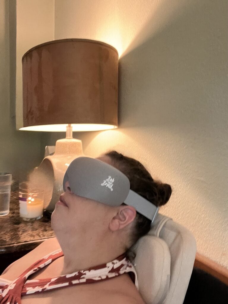 Woman relaxing with a sleep mask in a cozy room with warm lighting.