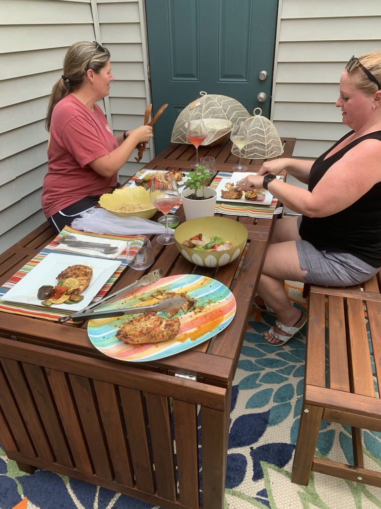 Two women enjoying a meal on a patio with colorful dishes and umbrellas.