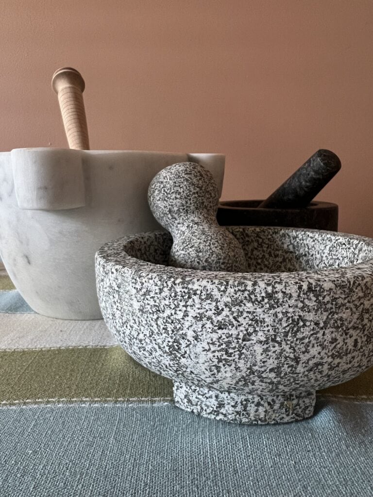 Elegant marble mortar and pestle set for kitchen use with a white bowl in background.