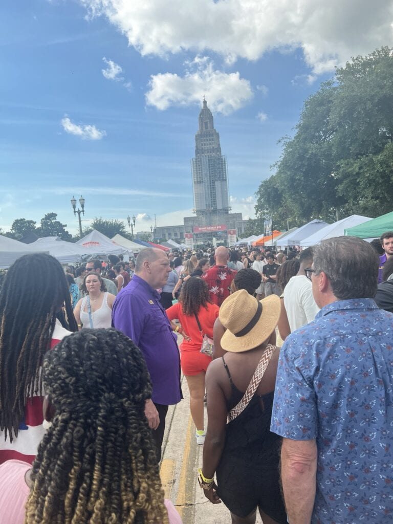 Crowd of people at outdoor festival with a tall building in the background.
