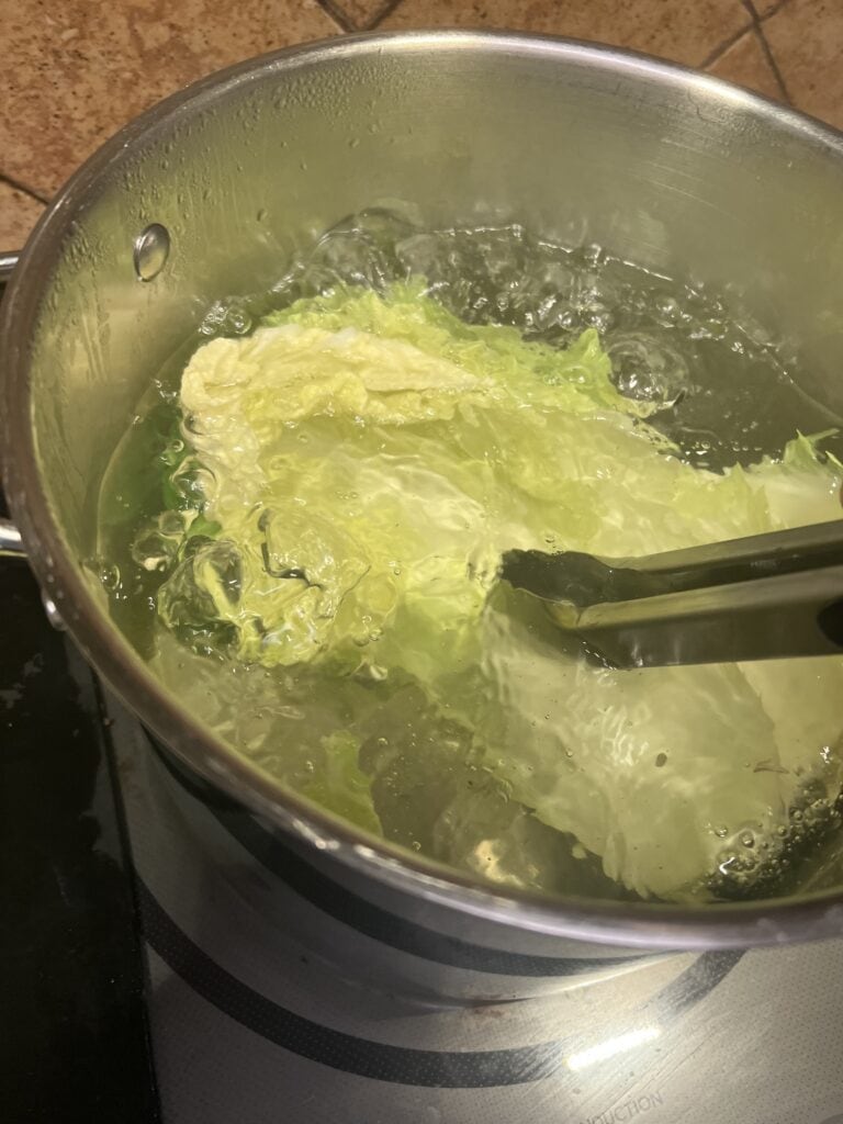 Lettuce boiling in a stainless steel pot on stove with tongs.