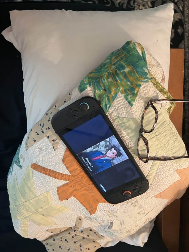 Decorative quilted pillow with smartphone and glasses on bed.