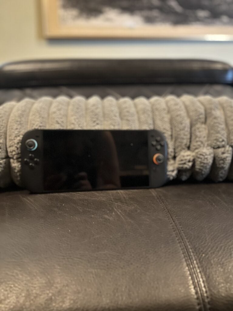 Nintendo Switch Lite gaming console on a leather surface with a blanket in background.