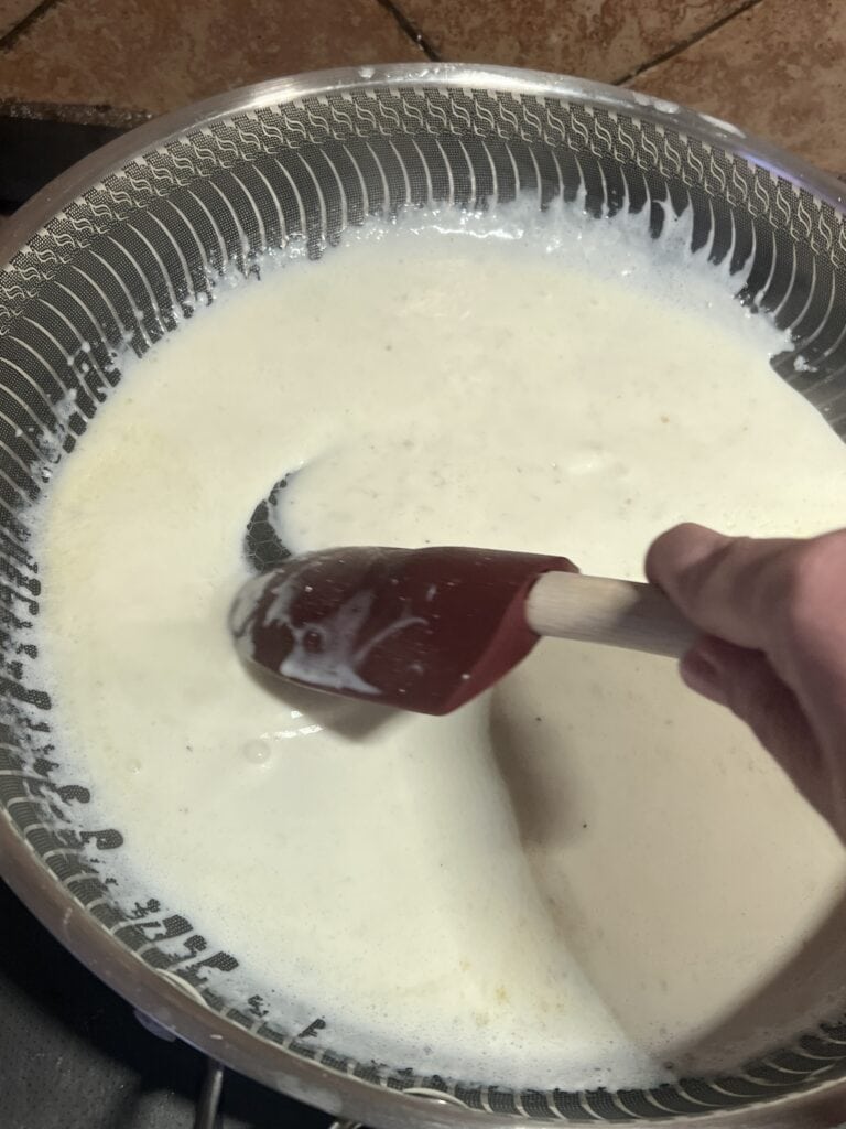 Cream sauce being stirred in a pan with a spatula for cooking or baking.