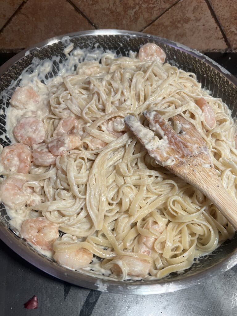 Delicious creamy shrimp fettuccine pasta in a silver pan with a wooden spoon.