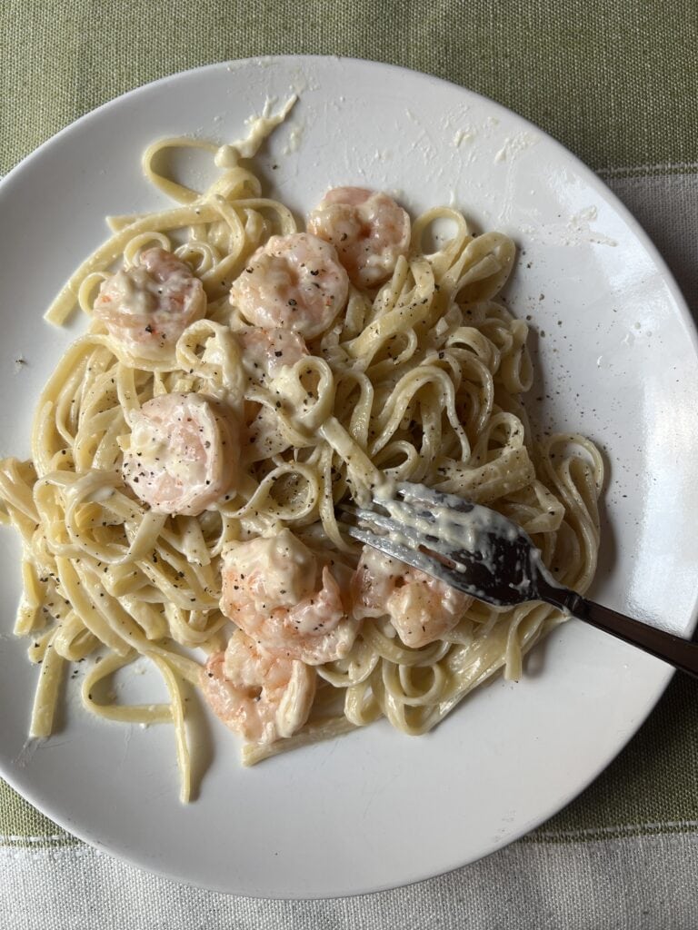 Creamy shrimp fettuccine Alfredo on white plate with fork, close-up.