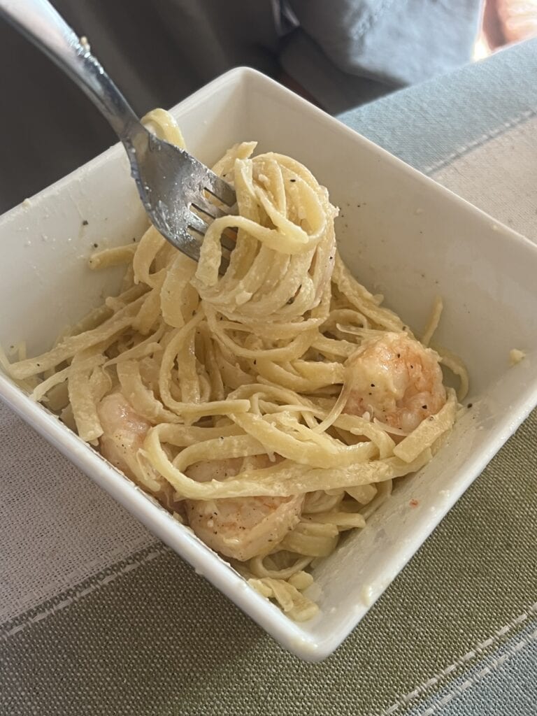 Close-up of creamy shrimp pasta in a white bowl with fork.