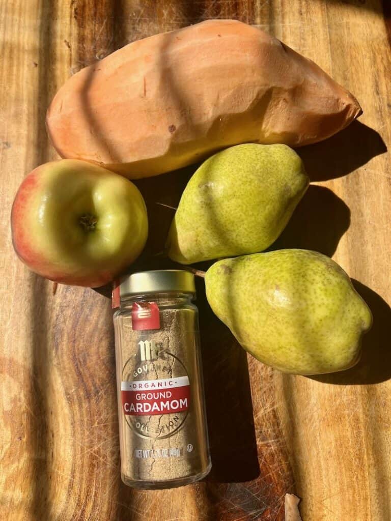 Fresh apples and pears with a bottle of ground cardamom on wooden surface.
