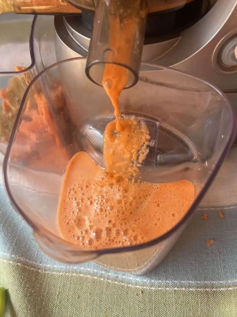 Smooth orange smoothie being dispensed into a glass from a juicer.