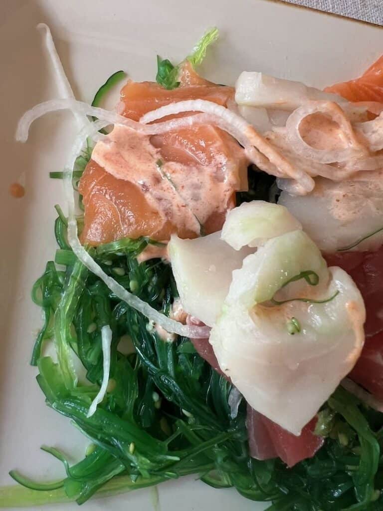 Fresh seaweed salad with sashimi and spicy mayo on a white plate.