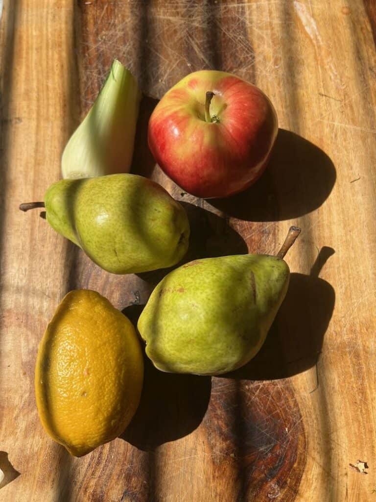 Assorted fresh pears, lemon, apple on wooden cutting board.