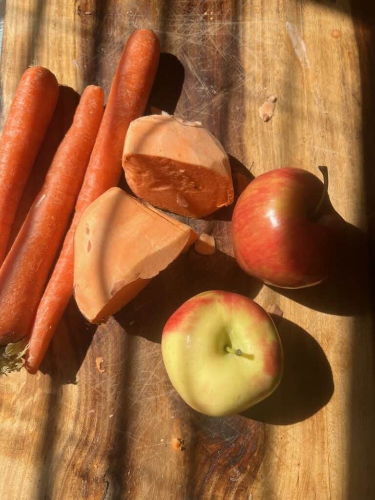 Carrots and apples on a wooden surface with sliced carrot pieces.