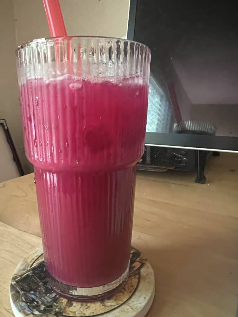 Bright magenta smoothie in a tall glass with a red straw on a wooden table.