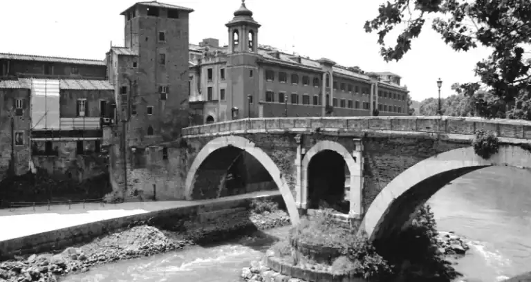Historic stone bridge over a river in a cityscape, black and white photo.