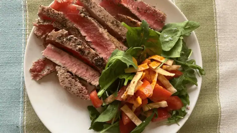 Juicy homemade steak with fresh greens and tomato salad on a white plate.