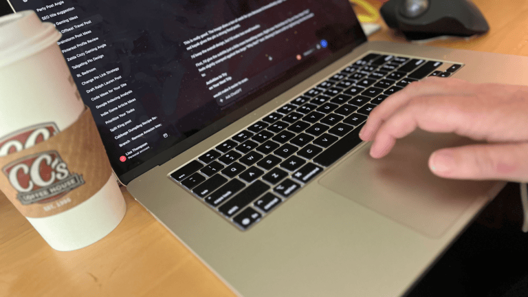 Person typing on a laptop with a coffee cup nearby, focused on digital content creation.