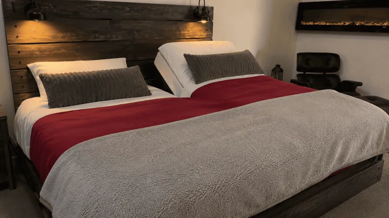 Cozy bedroom with wooden headboard, red and gray bedding, and ambient lighting.